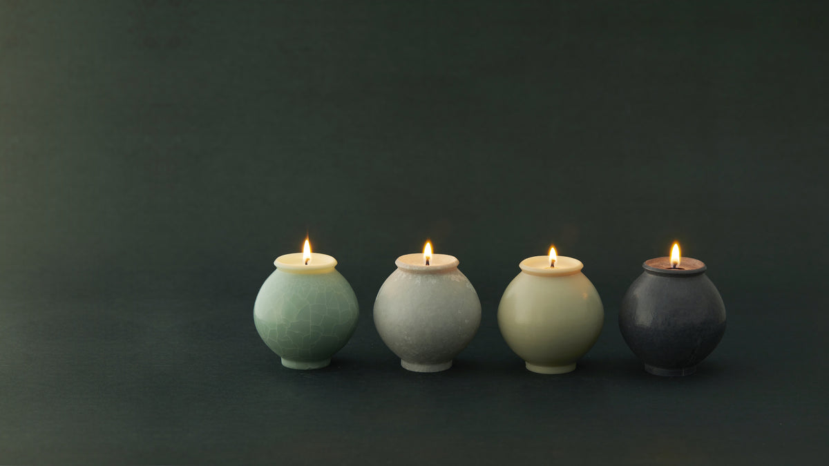 Four Unjo Mansion moon jar object candles lit on a dark green ground