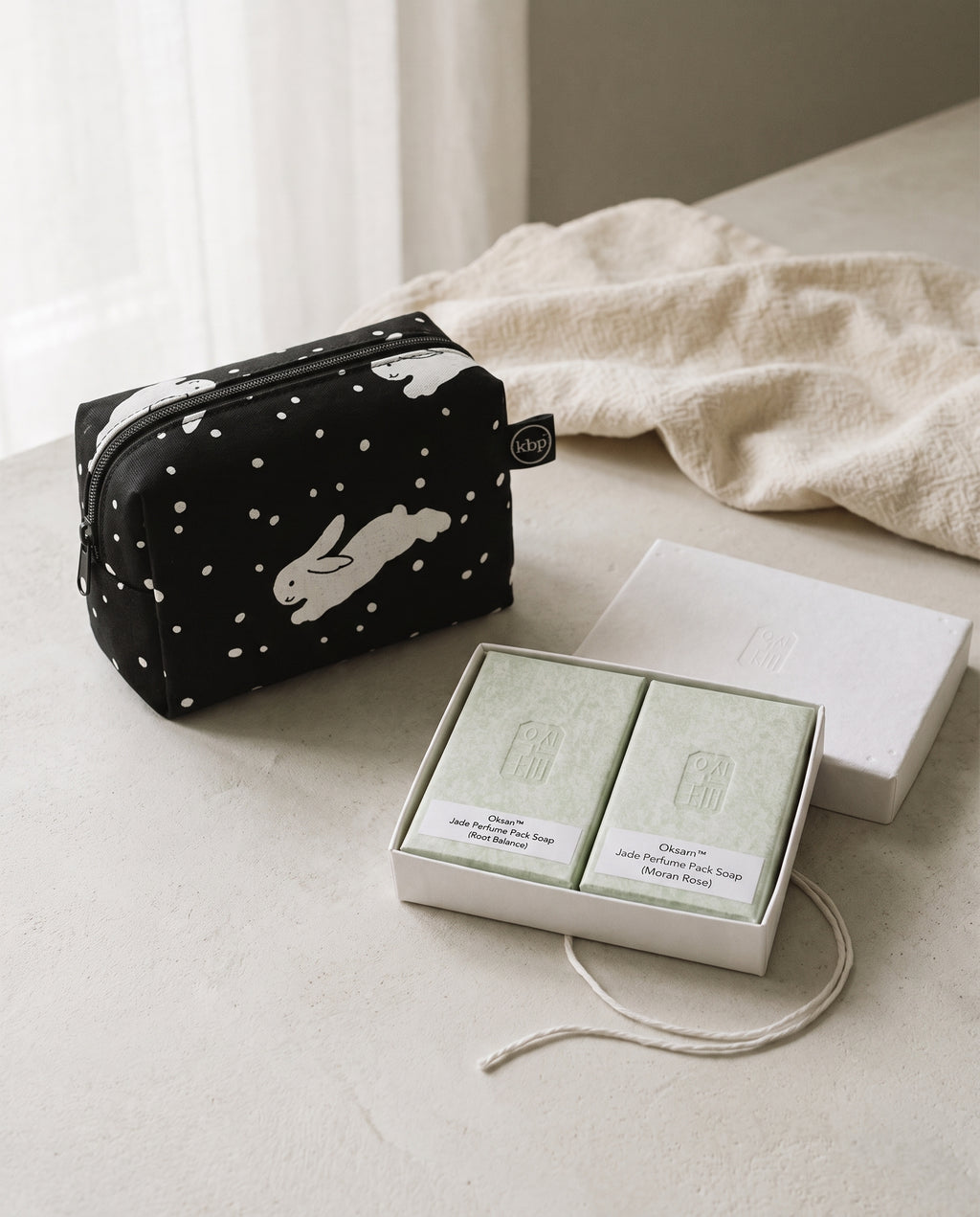 The Washbag Set in Snow Bunnies — black box pouch with a leaping white rabbit beside an open Oksan jade perfume soap duo