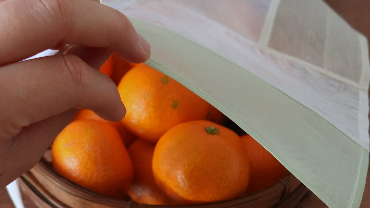 A hand lifting a YU:RÉE jogakbo silk cloth from a basket of mandarins