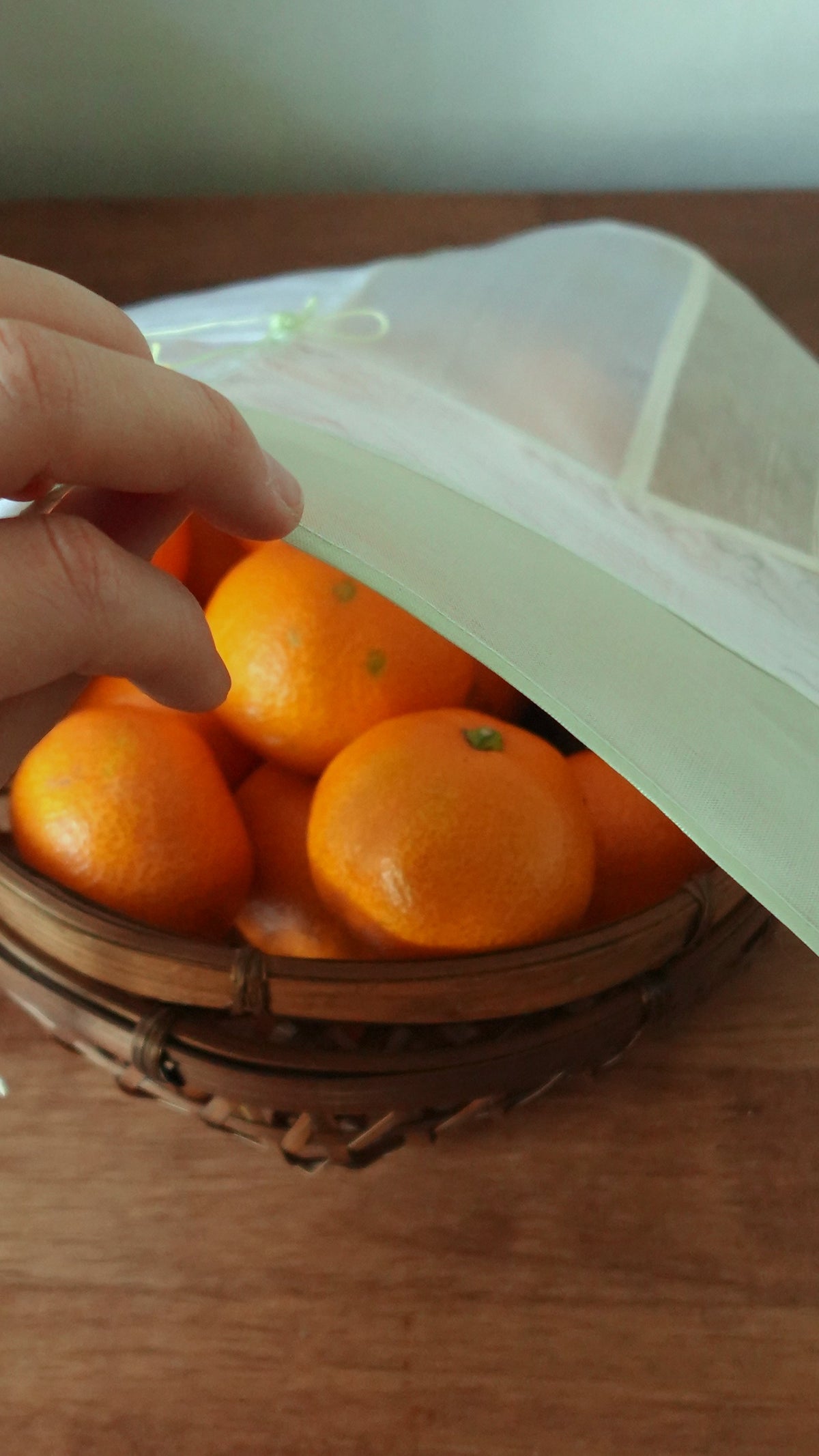 A hand lifting a YU:RÉE jogakbo silk cloth from a basket of mandarins